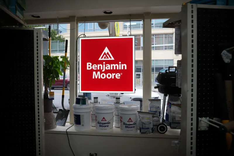 An illuminated Benjamin Moore dealer sign beside stacked paint buckets