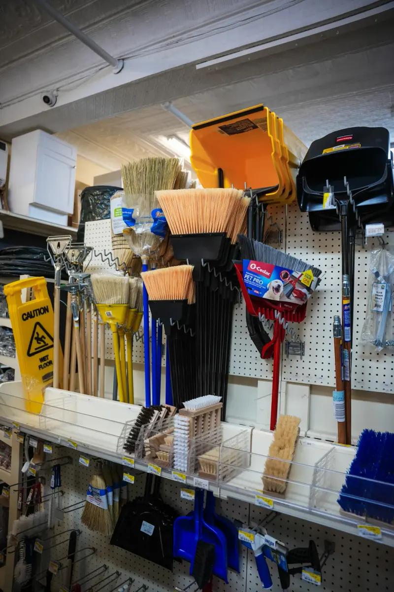 Brooms, squeegees and dustpans hanging on a pegboard beside a wet-floor sign