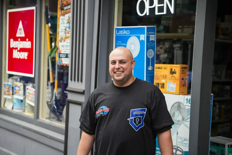 Mike, the owner of Yonkers Paint & Hardware, smiling outside the store entrance